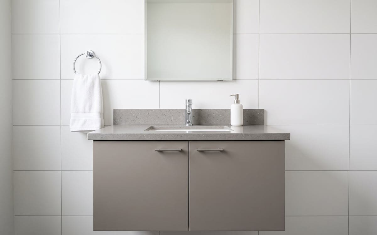 A wall-hung gray vanity in a guest bath, with a white soap pump by the chrome faucet and a fresh hand towel on the ring.
